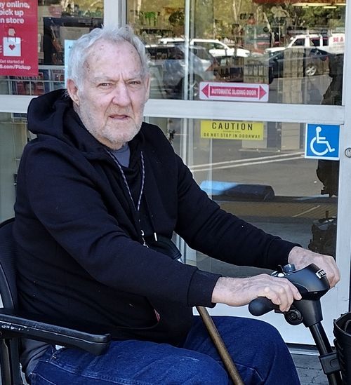 John sitting in an electric wheelchair in front of a store.