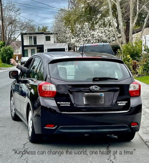 Rear view of a black Subaru hatchback as it drives away with the driver waving