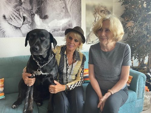 A dog and two women sit on a couch with the women looking at the dog